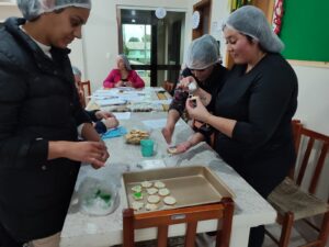 Mulheres em aventais preparando biscoitos em uma mesa de cozinha